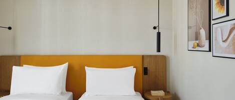 A hotel room with two beds, a wooden headboard, a nightstand, and two framed pictures on the wall.