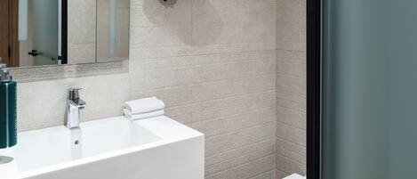 A modern bathroom with a white sink, a round mirror, and a glass shower enclosure.