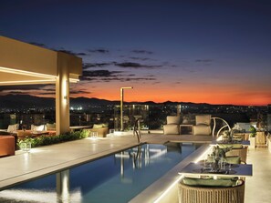 A rooftop pool area with seating and a view of the city at dusk. - Hilton Garden Inn Chania City (Chania)