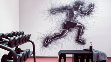 A gym with a wall mural of a dynamic figure, a dumbbell rack, and a piece of exercise equipment.