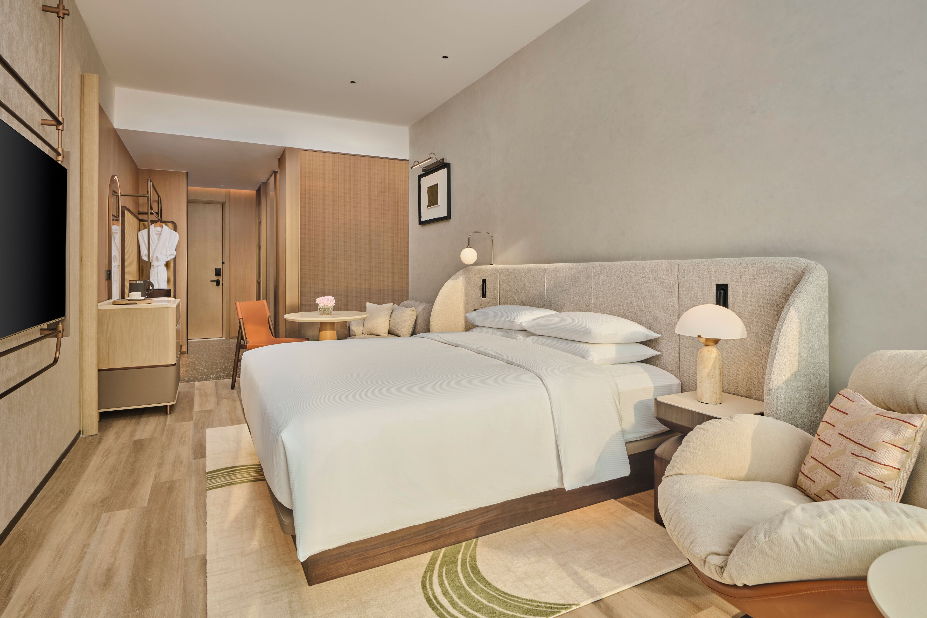 Una habitación de hotel moderna con una cama grande, mesitas de noche, televisor y baño con espejo y toallero.