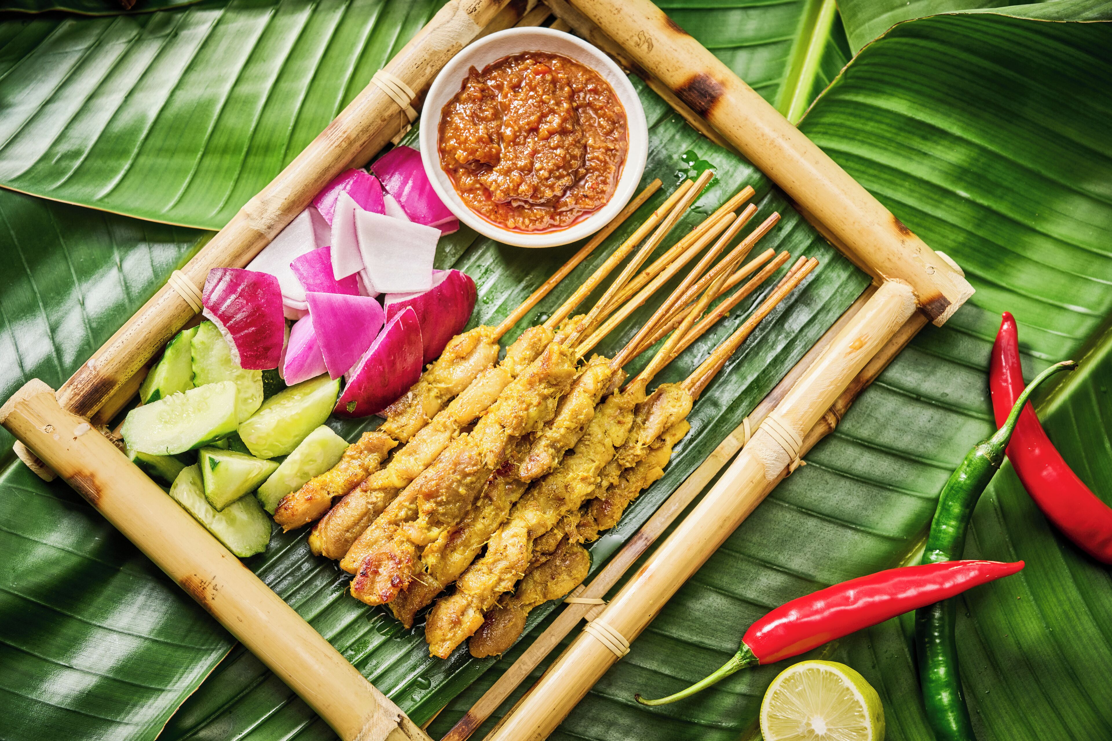 A traditional Southeast Asian dish with skewers, pickled vegetables, and a dipping sauce on a banana leaf.