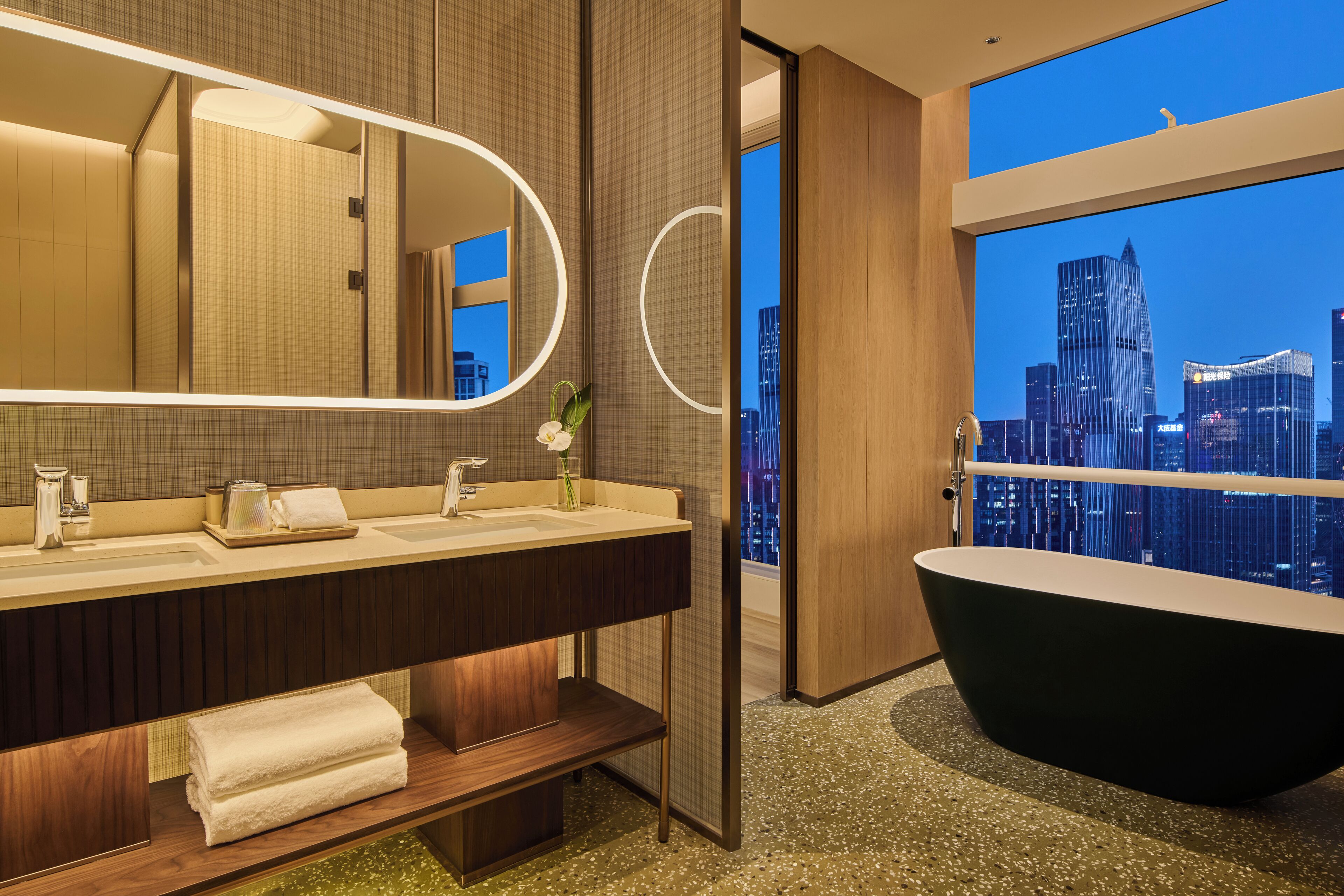 A modern bathroom with a large mirror, two sinks, a bathtub, and a city view.