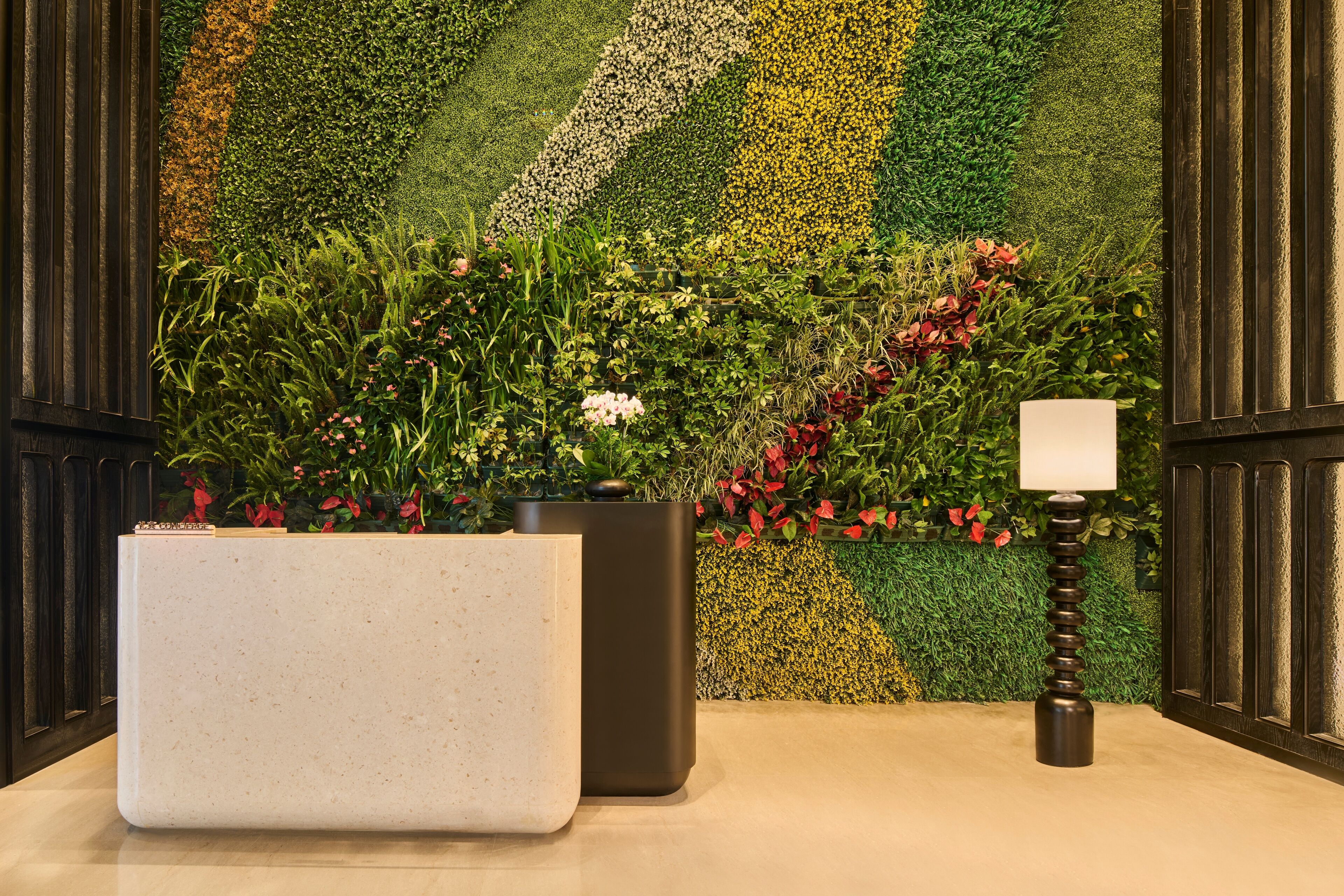 A reception area with a modern design, featuring a large white reception desk, a dark-toned lamp, and a wall with a green and yellow patterned backdrop.
