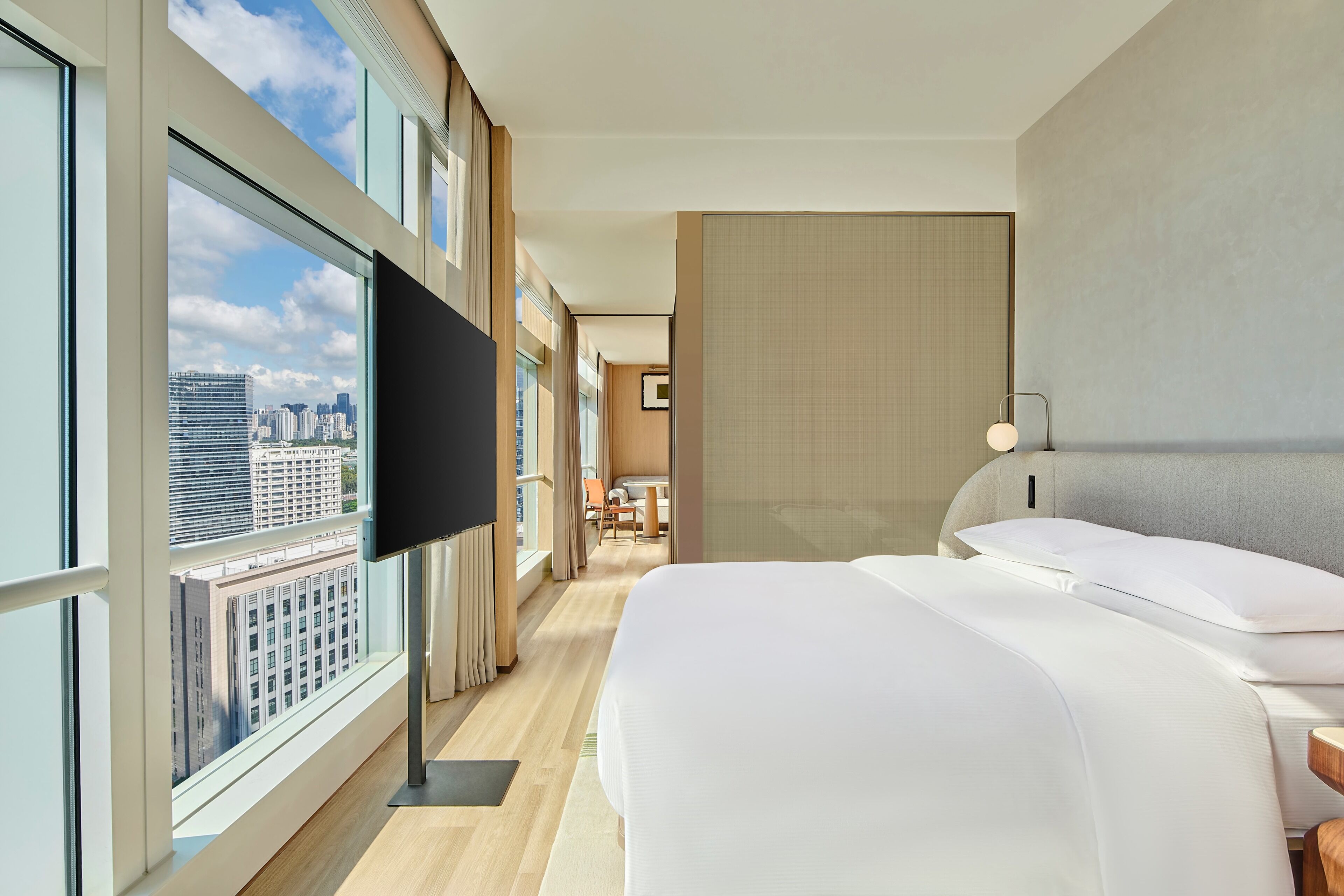 A hotel room with a large window, a flat-screen TV, two beds, and a view of the cityscape.