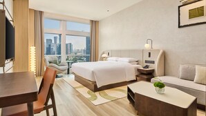 A modern hotel room with a large bed, a sofa, a dining table, and a city view. - Doubletree By Hilton Shenzhen Bay (Shenzhen)