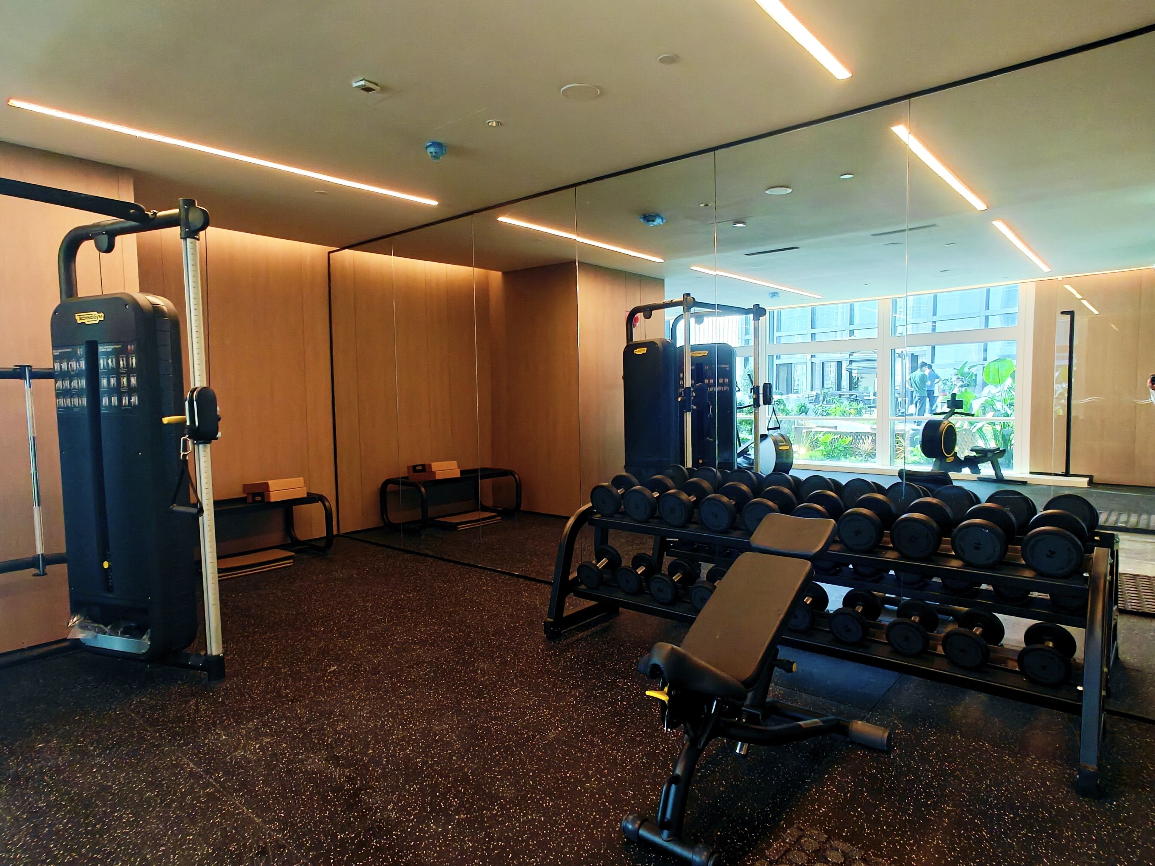 Una palestra con attrezzature per esercizi, rastrelliere per pesi e un'ampia finestra che offre vista all'esterno.