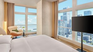 A hotel room with a large bed, a chair, a small table, and a TV. The room has large windows with a city view. - Doubletree By Hilton Shenzhen Bay (Shenzhen)