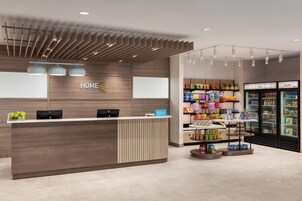 A hotel reception area with a wooden reception desk, two HP computers, a blue Hilton Honors sign, and a snack display.