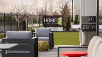 Un patio con mobiliario exterior, una parrilla y vistas a una propiedad privada.