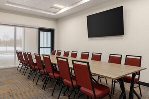 A conference room with a long table and red chairs, a large screen on the wall, and a view through a window. - Home2 Suites By Hilton Vaughan Toronto On (Vaughan)