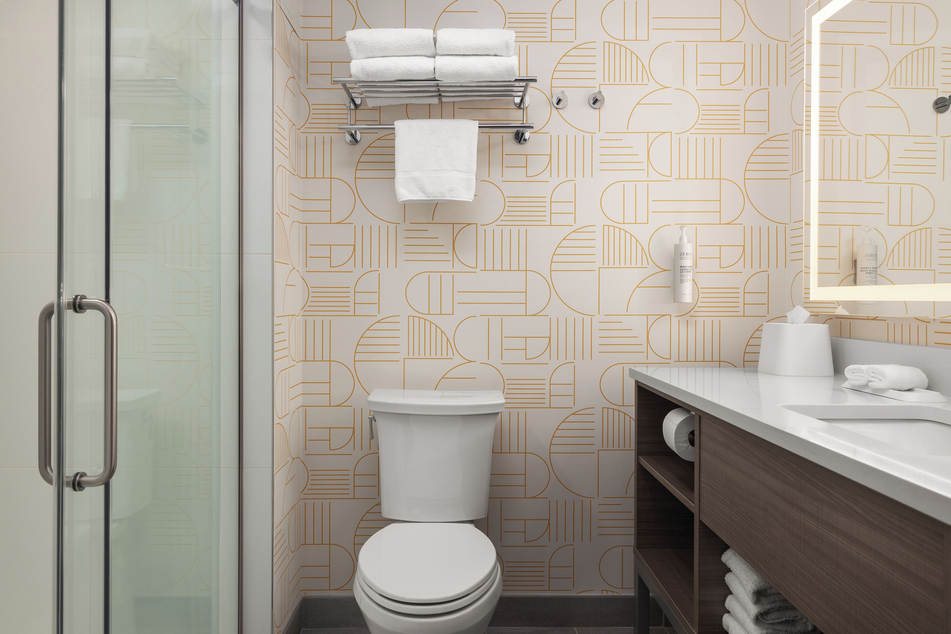 Une salle de bain moderne comprenant des toilettes, une douche à parois de verre, un porte-serviettes et un meuble-lavabo avec un miroir.