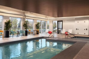 An indoor swimming pool with clear glass walls, a tiled floor, and a few lounge chairs. - Home2 Suites By Hilton Vaughan Toronto On (Vaughan)