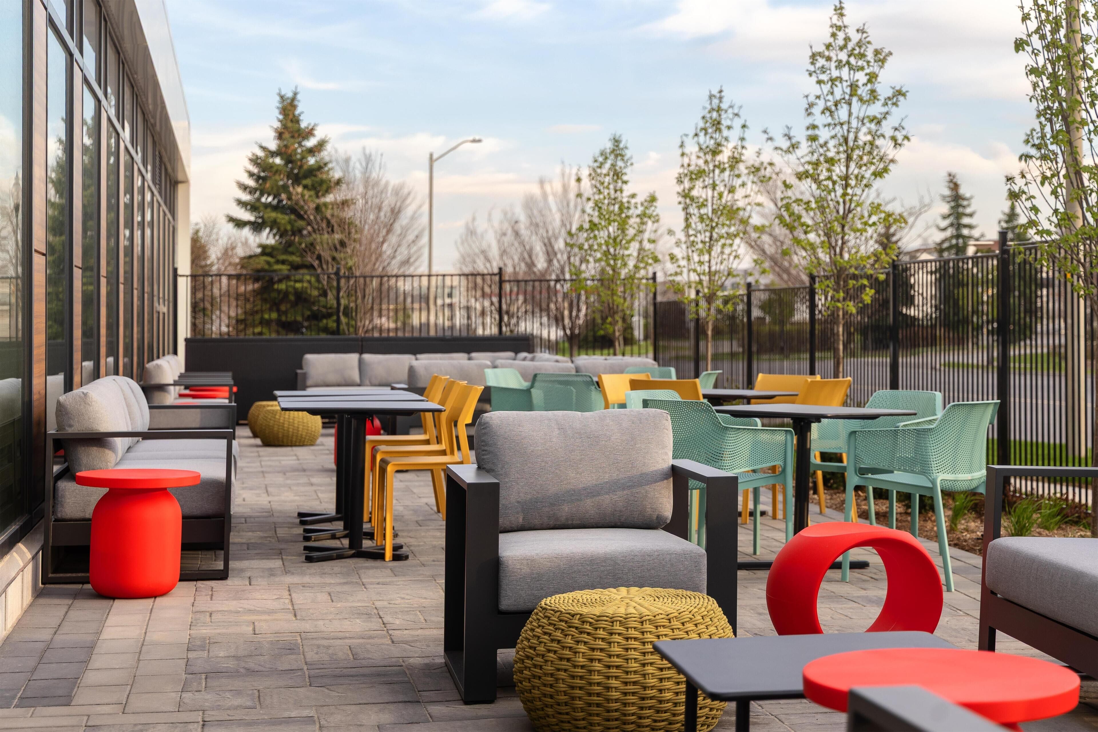 An outdoor seating area with tables and chairs, a sofa, and a red stool.