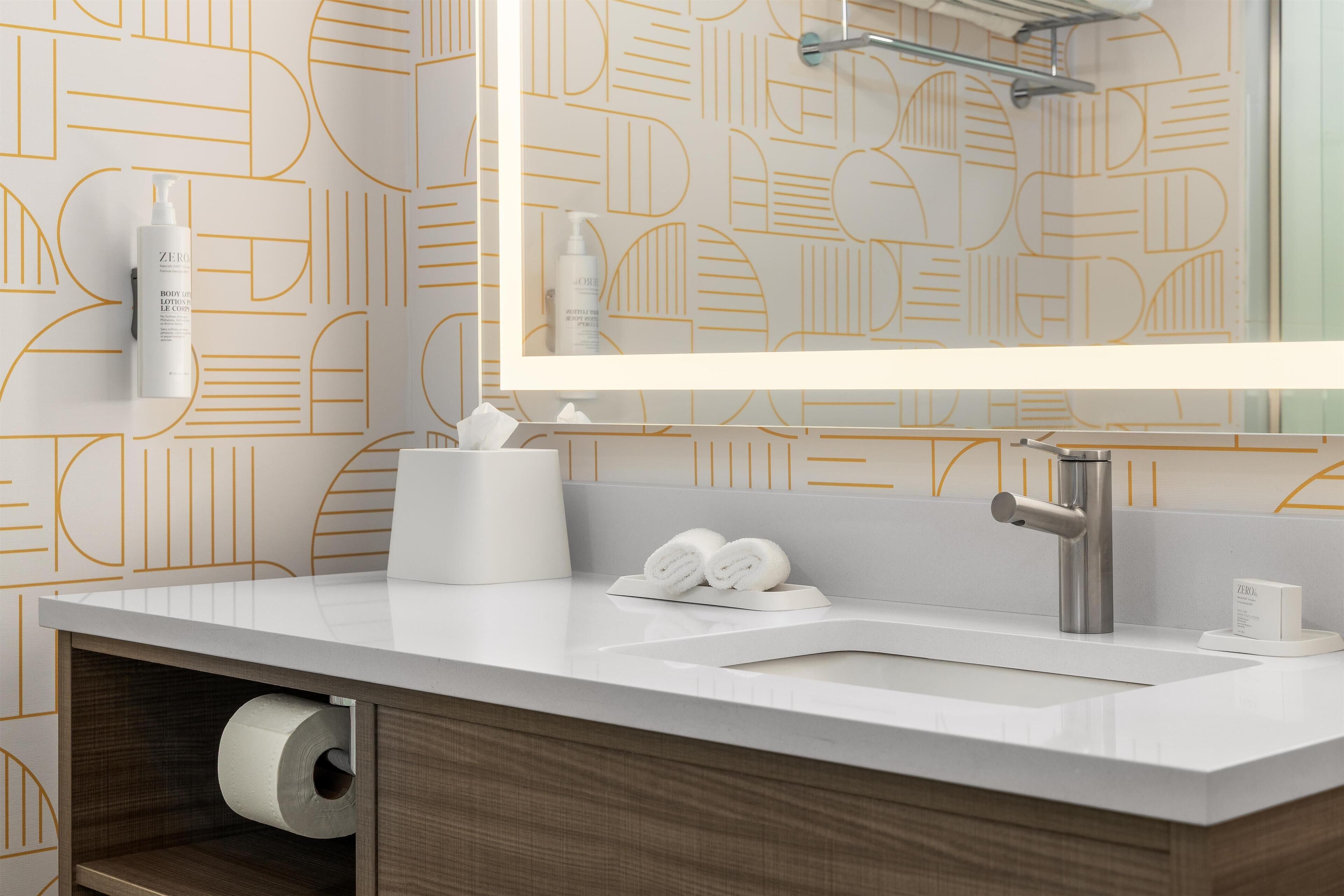 Un baño moderno con tocador blanco, un espejo grande y papel tapiz con estampado geométrico.