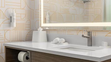 Un baño moderno con tocador blanco, un espejo grande y papel tapiz con estampado geométrico.