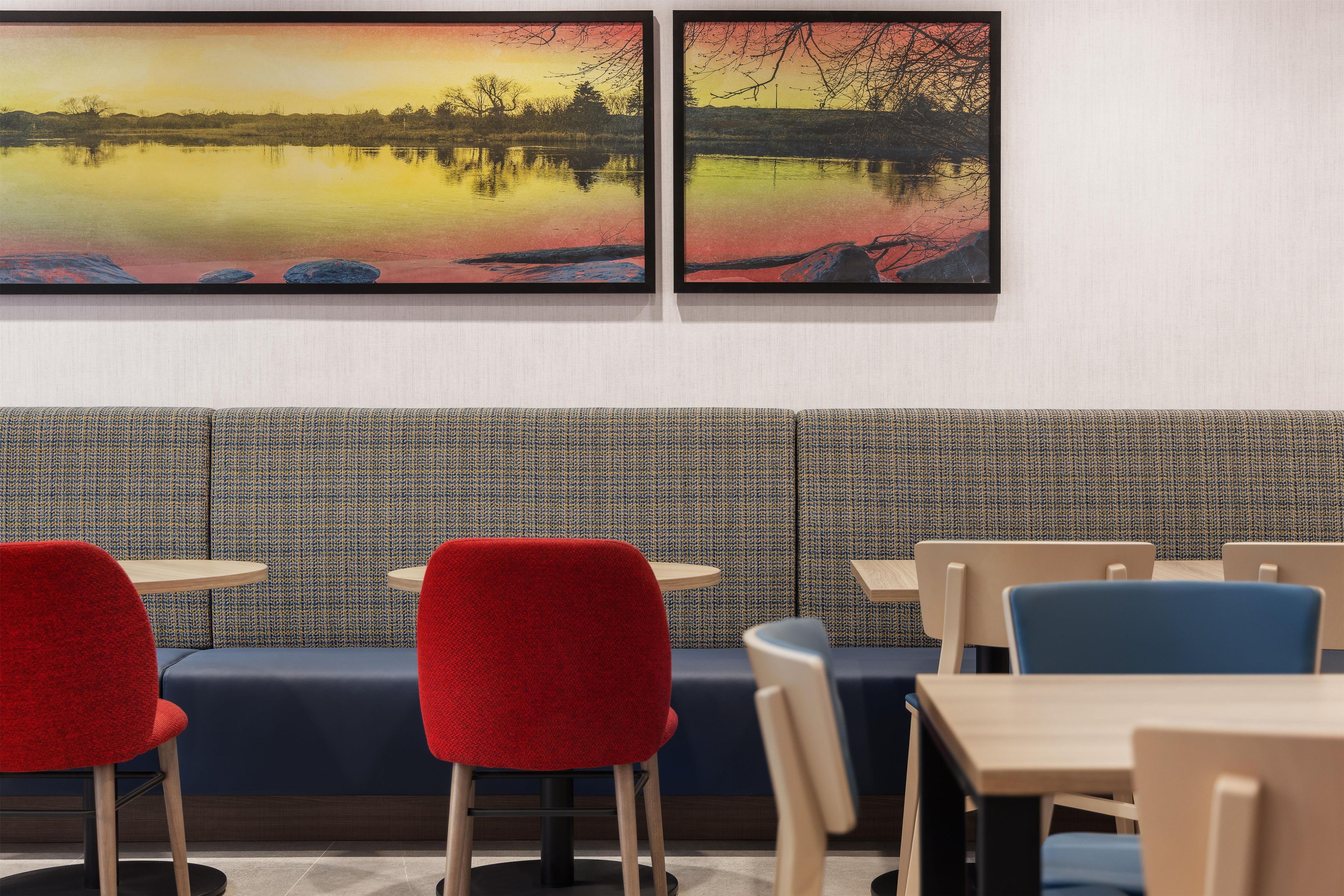 A dining area with a patterned wall, a blue cushioned bench, and red and blue chairs.