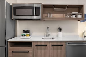 Una cocina moderna con microondas integrado, pileta de acero inoxidable y muebles de madera.