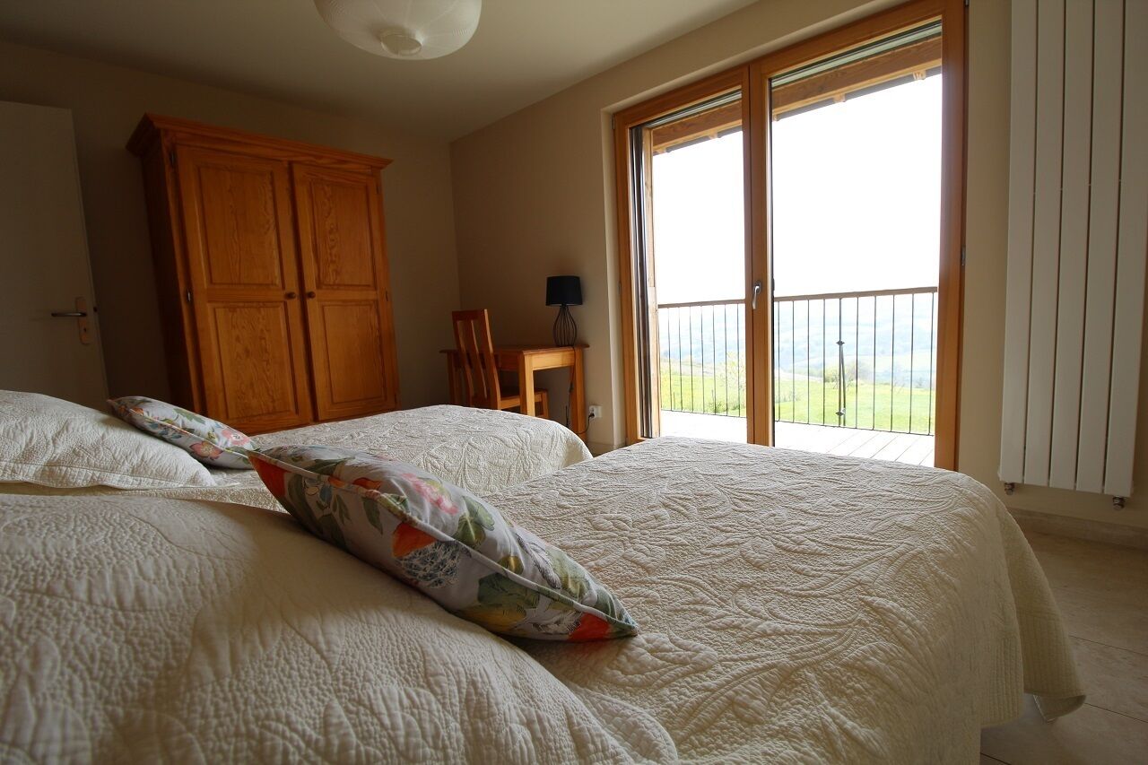 Un dormitorio con una cama grande, un armario de madera, una mesita con una lámpara y un balcón con vistas.