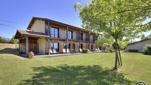 A two-story building with a wooden facade and a balcony. There are several lounge chairs arranged in front of the building. - Gîte des Buis du Chardonnet (COGNY)