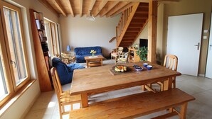 A spacious living area with a wooden dining table, blue sofa, and a staircase leading to another level. - Gîte des Buis du Chardonnet (COGNY)