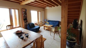 A cozy living room with a wooden ceiling, a blue sofa, a dining table with chairs, and a bookshelf. - Gîte des Buis du Chardonnet (COGNY)