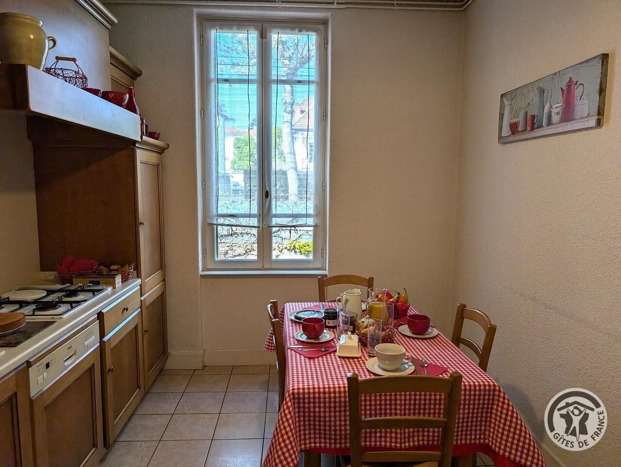 Eine Küche mit einem Esstisch, der für das Frühstück gedeckt ist, einem Fenster mit Vorhängen und einem Bild an der Wand.