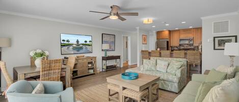 A spacious living room with a large TV, comfortable seating, a dining area, and a kitchen.