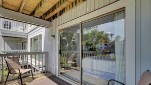 Un espace extérieur abrité doté d’une terrasse en bois, de deux chaises et d’une porte vitrée donnant accès à une zone piscine.