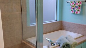 Un baño con ducha de vidrio, un lavamanos con espejo y un perchero con una toalla decorativa.