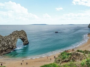 A coastal scene with a prominent rock arch formation, a sandy beach, and a calm sea.