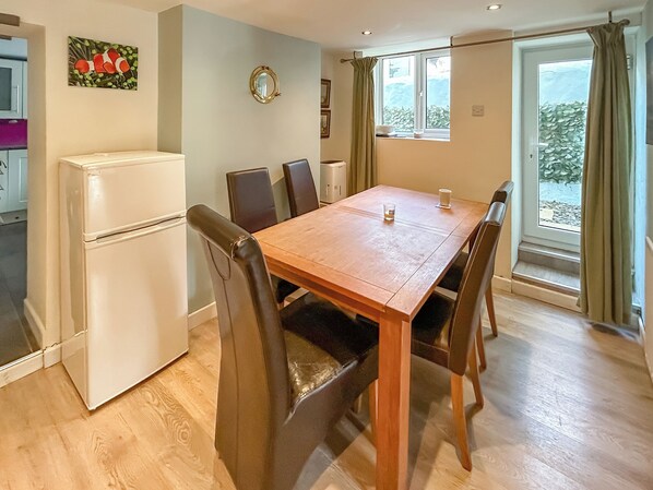 A dining area with a wooden table and chairs, a white refrigerator, and a window with curtains.