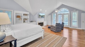 Un'ampia camera da letto con un letto grande, un caminetto, una TV e vista sull'esterno attraverso le finestre.