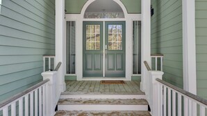 Un portico con una porta verde, ringhiere bianche e una scala in legno.