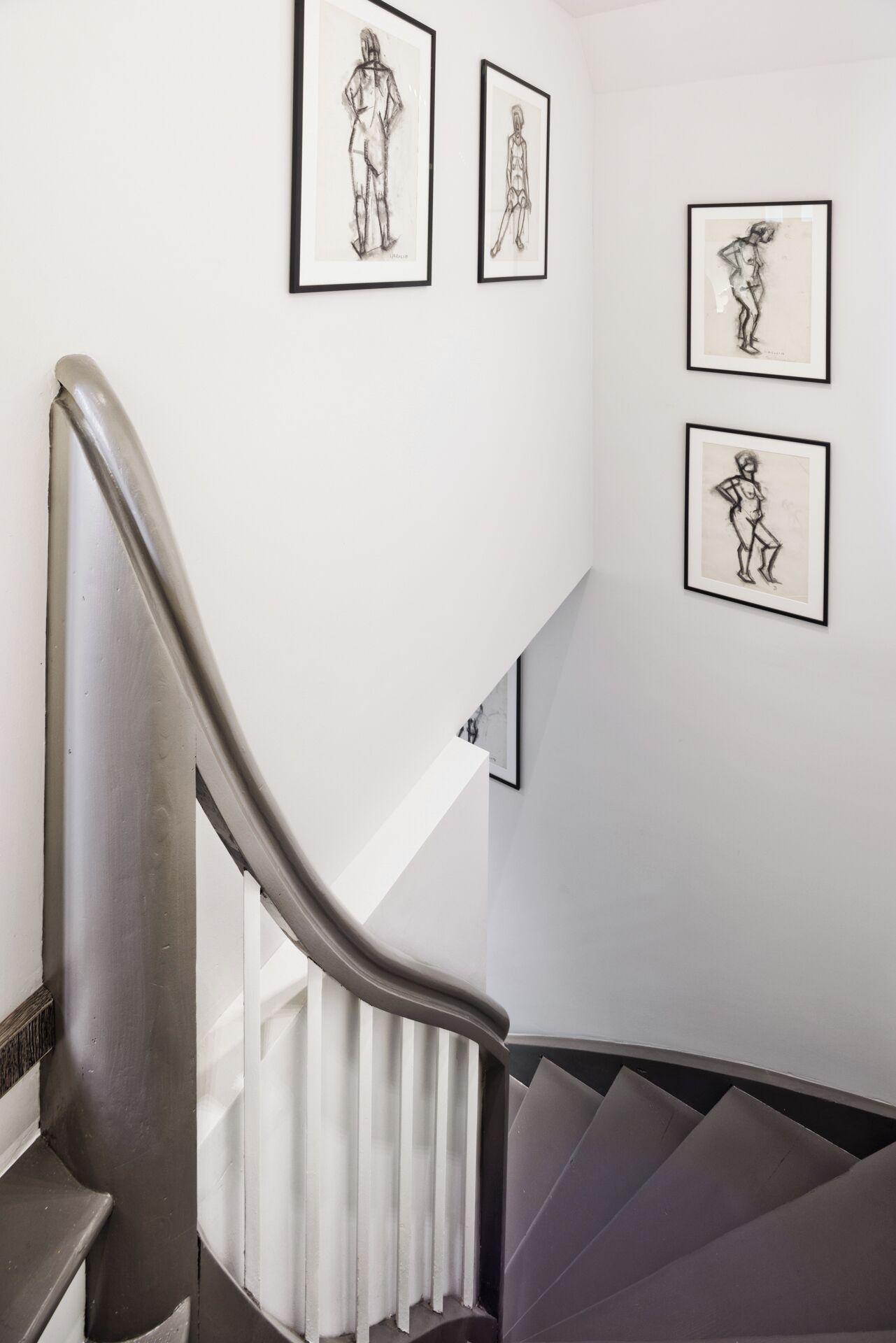 Eine Treppe mit Metallgeländern und einer weißen Wand mit in Bilderrahmen gefassten schwarz-weißen Skizzen von Menschen.