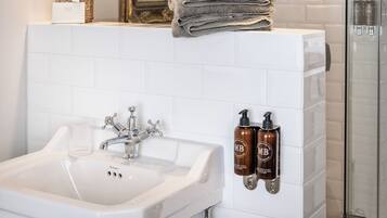 A bathroom with a white sink, two pendant lights, a framed painting, and a stack of towels.