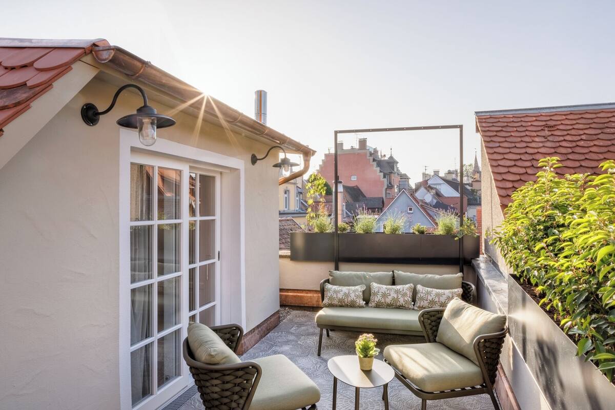 Terraza en la azotea con zona de estar, puerta de cristal y vistas de edificios circundantes.