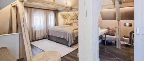 Un dormitorio con cama, una mesita de noche, una silla y una ventana con cortinas.