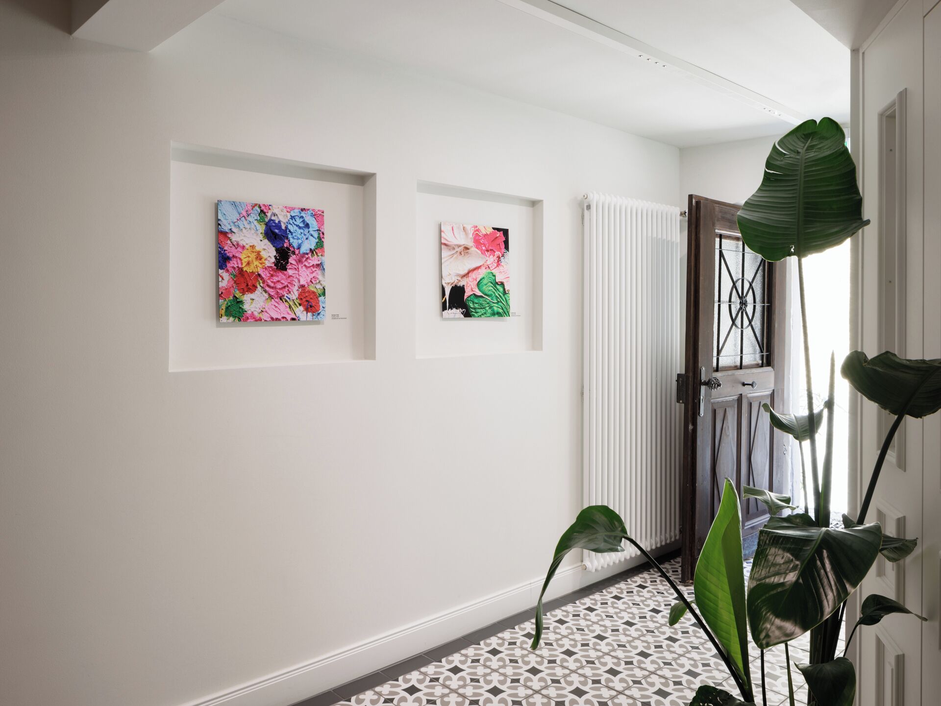 A hallway with two framed floral artworks on the wall, a radiator, and a potted plant.