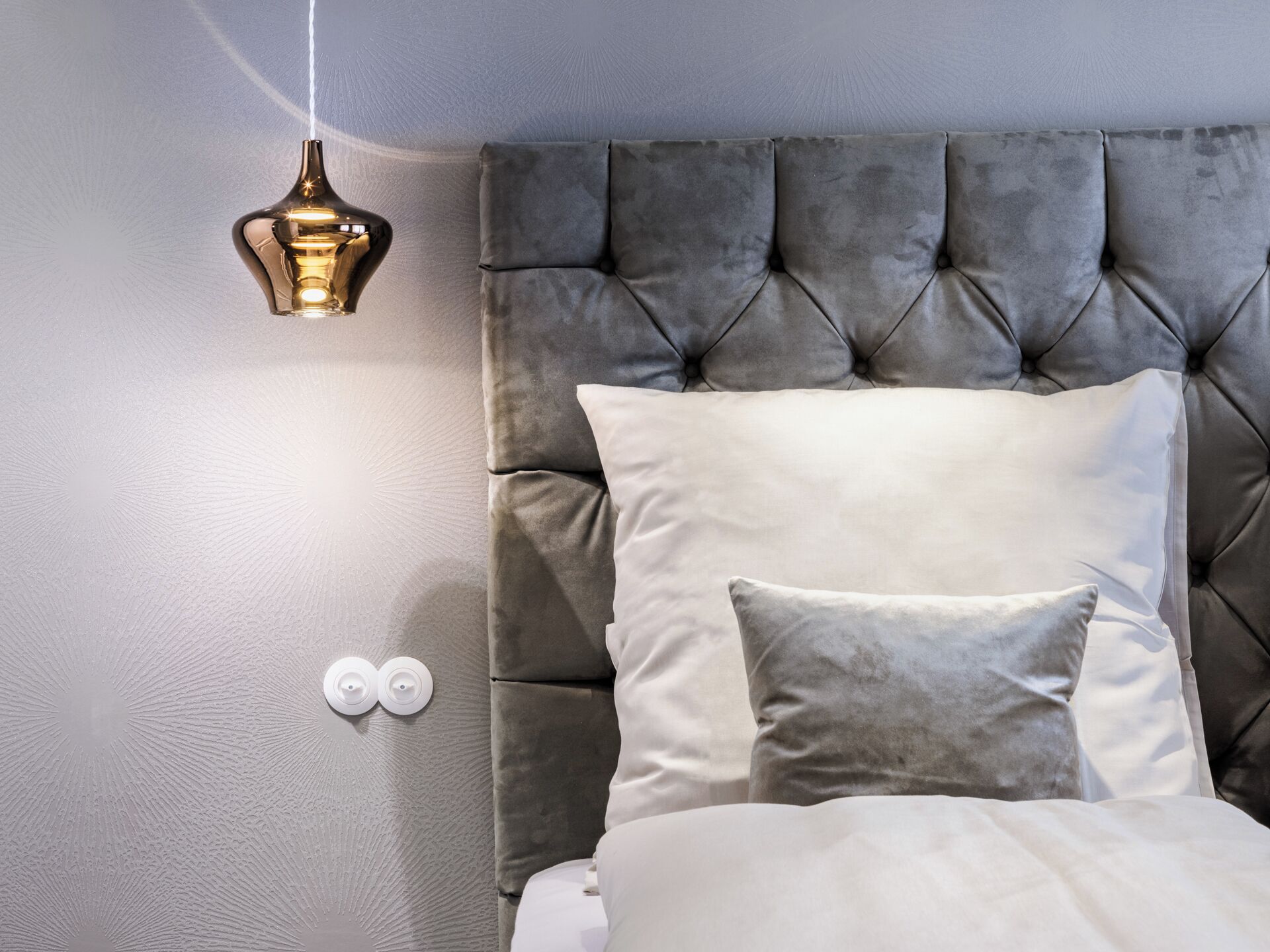 A bedroom with a tufted headboard, a hanging light fixture, and a bed with white bedding.
