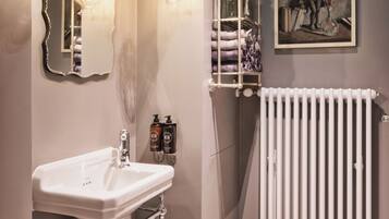 Un baño con un lavabo blanco, un espejo, un radiador y un cuadro en la pared.