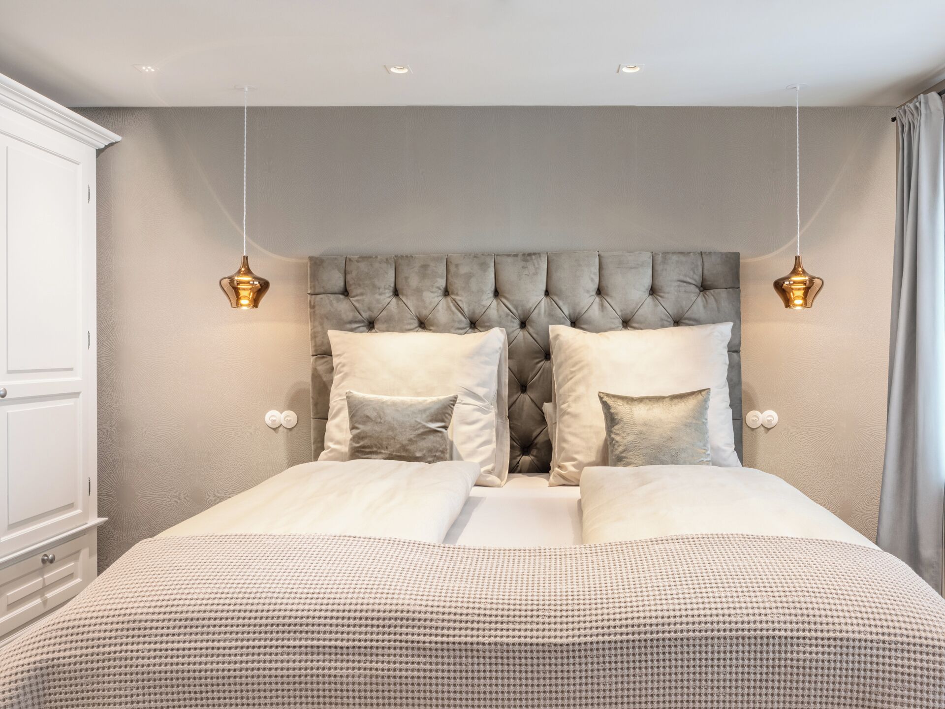 A bedroom with a tufted headboard, two bedside lamps, and a large bed with multiple pillows.