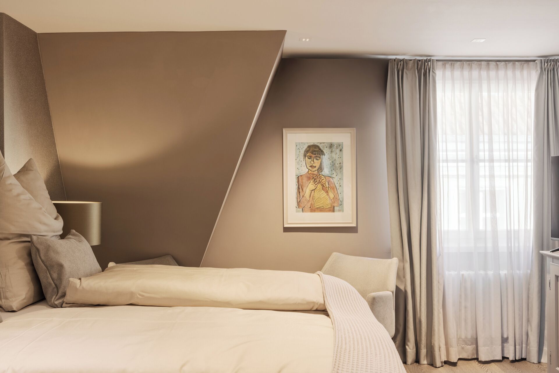 A modern bedroom with a bed, pillows, a framed artwork, and sheer curtains.