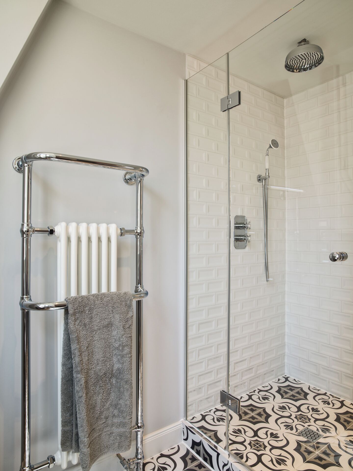 Un baño moderno con cabina de ducha de vidrio, un perchero de toallas cromado y baldosas de suelo con estampado.