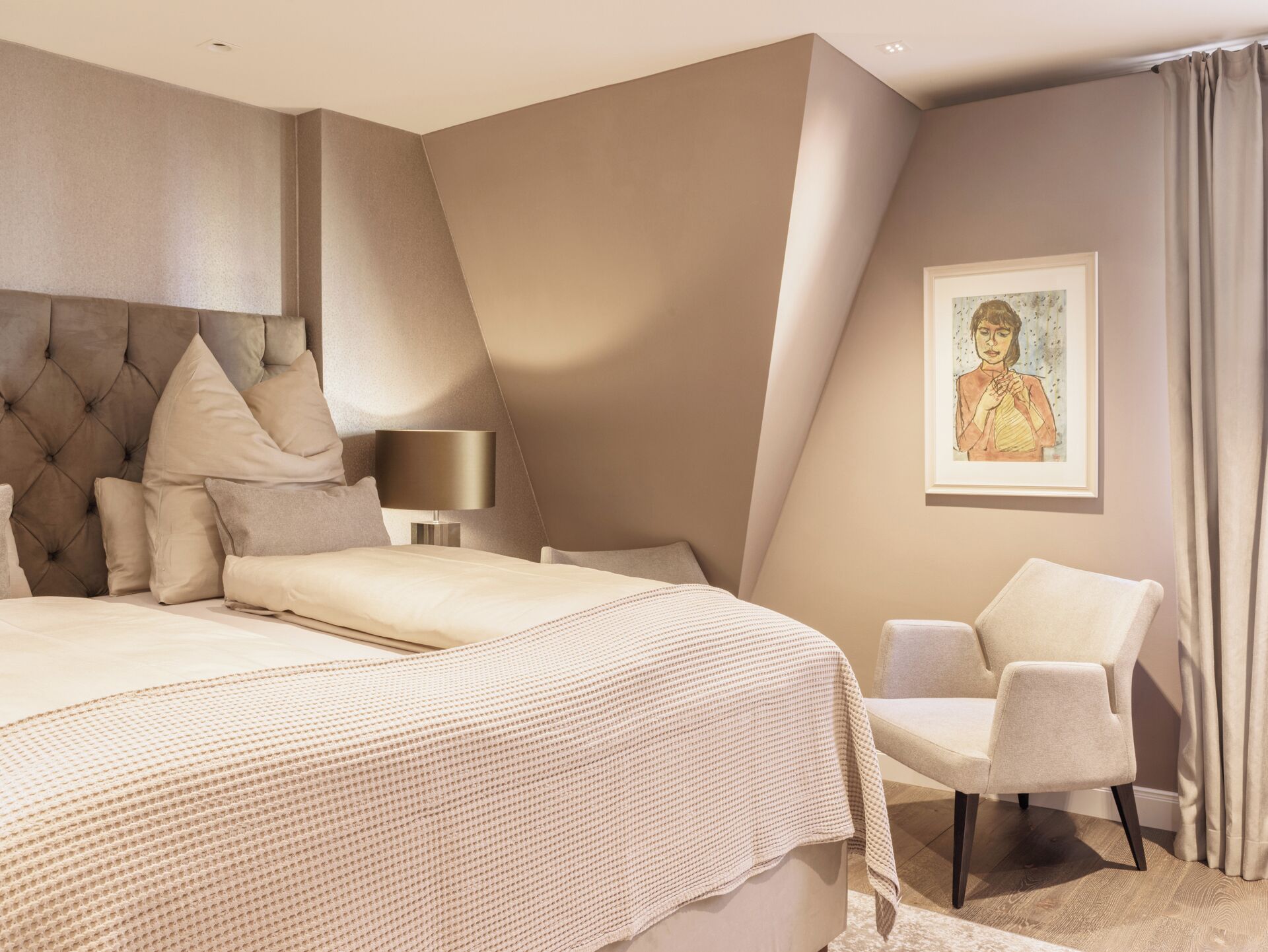 Ein modernes Schlafzimmer mit einem großen Bett, einem Nachttisch, einem Sessel und einem gerahmten Bild an der Wand.