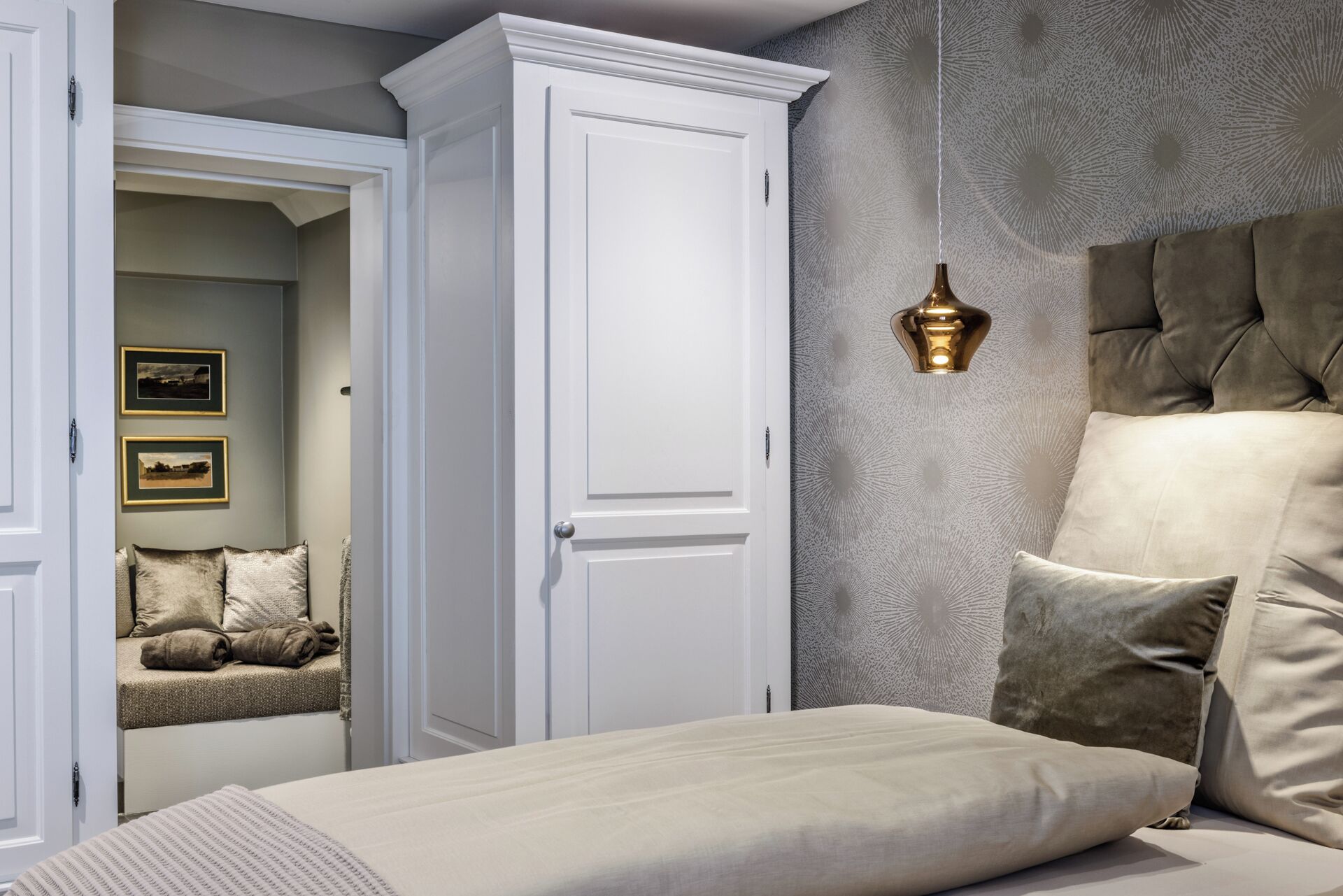 A bedroom with a bed, a wardrobe, a wall-mounted light fixture, and two framed pictures on the wall.