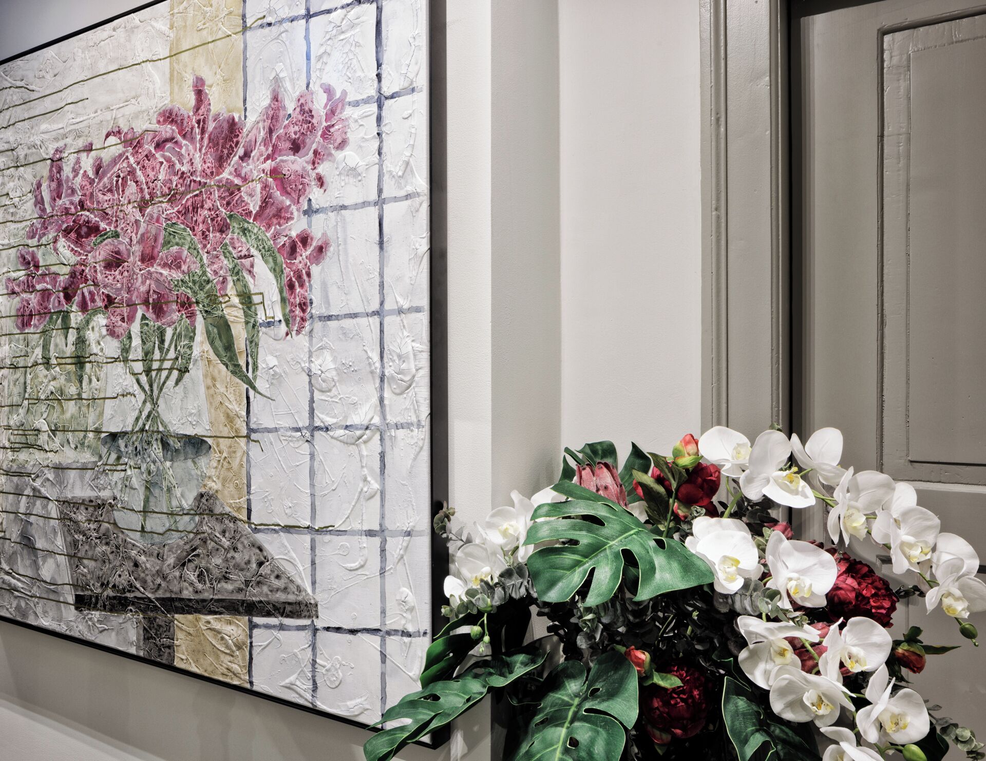 Una pared con una pintura de textura que muestra flores rosas y un jarrón con orquídeas blancas y rojas.
