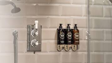 Zona de ducha con pared de azulejos, ducha de mano, grifo de pared y tres botellas de champú.