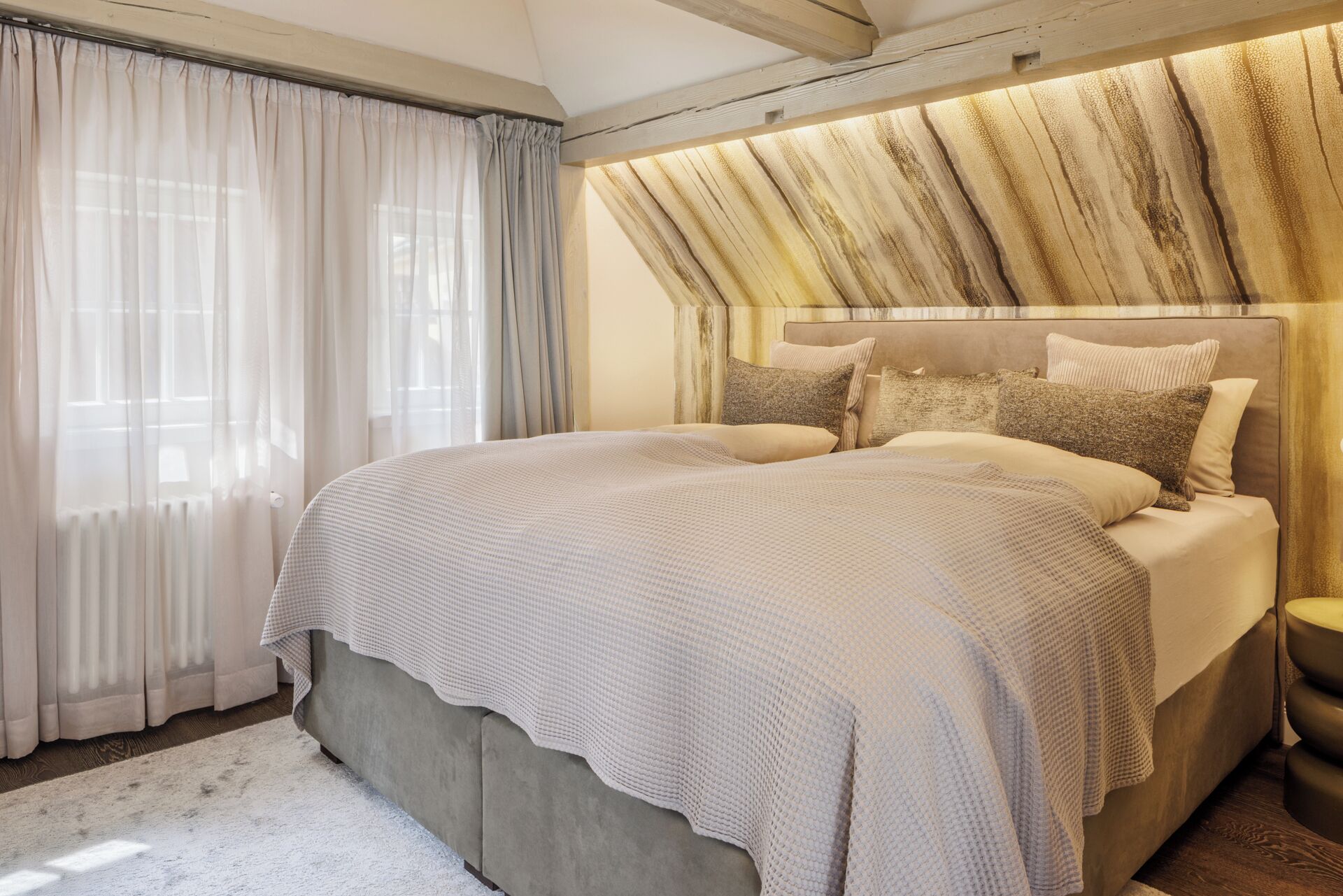 A bedroom with a large bed, a headboard with a textured design, and a window with sheer curtains.