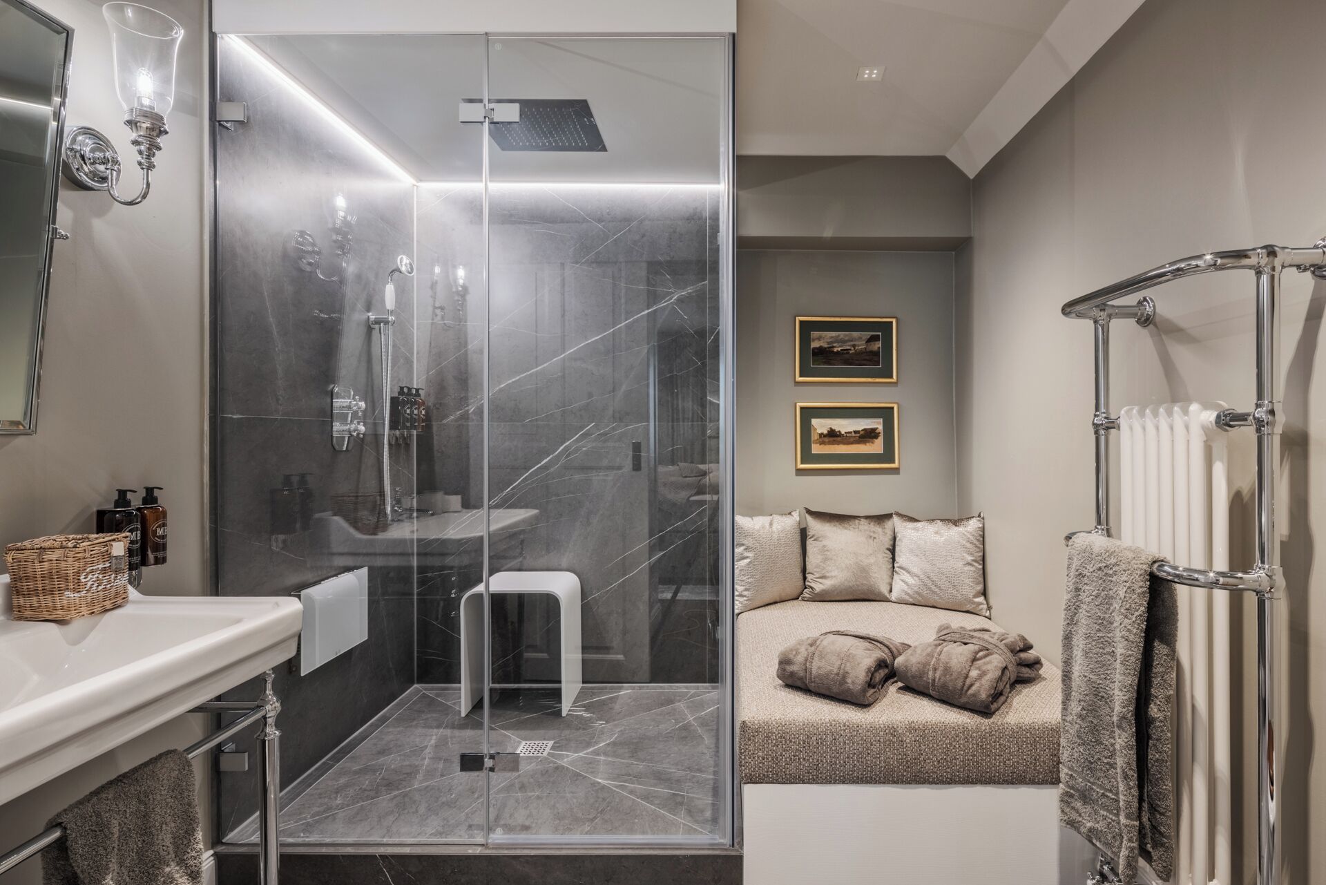 A modern bathroom with a glass-enclosed shower, a white sink, and a bathtub. There are two framed pictures on the wall, a towel rack, and a basket on the counter.